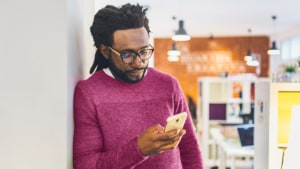 A man laying against wall holding and looking at his phone.