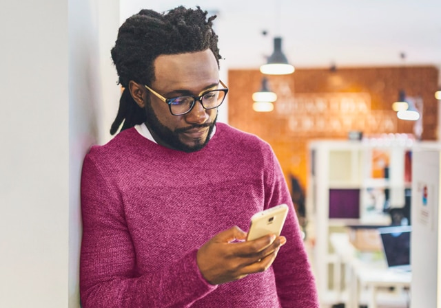 A man laying against wall holding and looking at his phone.