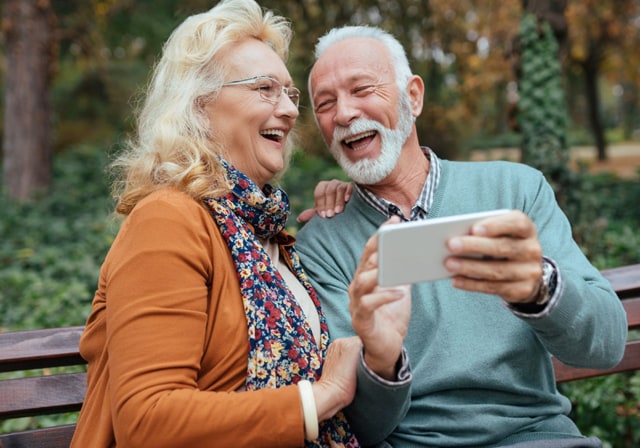 Two seniors laughing together while one of them holds a smartphone in front of them.