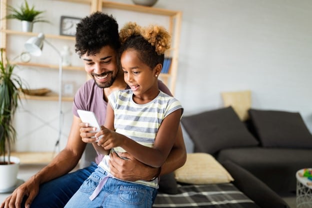 Dad and child sitting on a couch holding and smiling at an ipad