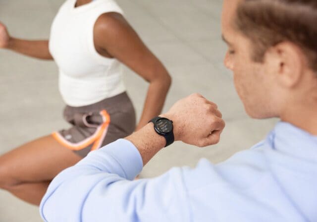 Man checking his Google Pixel Watch, while a girl in the back is doing a workout.