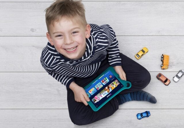 A smiling child looking upward while holding a tablet.